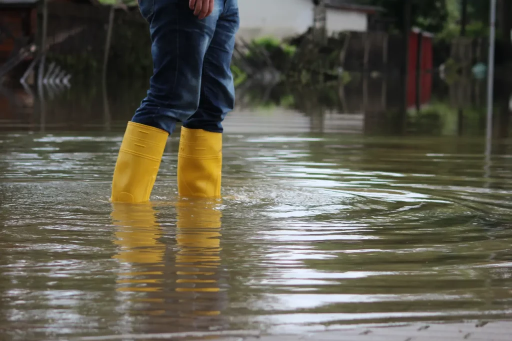 A close up of a person wearing yellow boots walking through standing water.